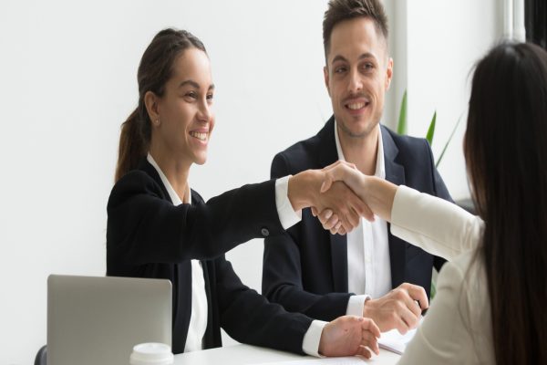 Smiling HR managers greeting female job applicant with handshake during recruiting or interview. Businesswoman making good first impression shaking hands of business partners. Partnership, cooperation